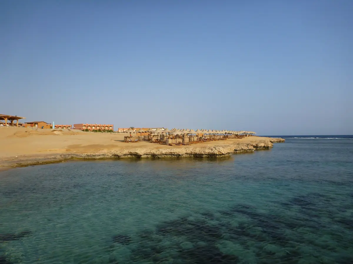 Shallow clear bay with a low rocky shoreline and buildings in the distance