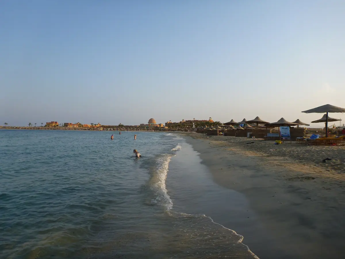 Sandy beach with straw sunshades along calm shallow water